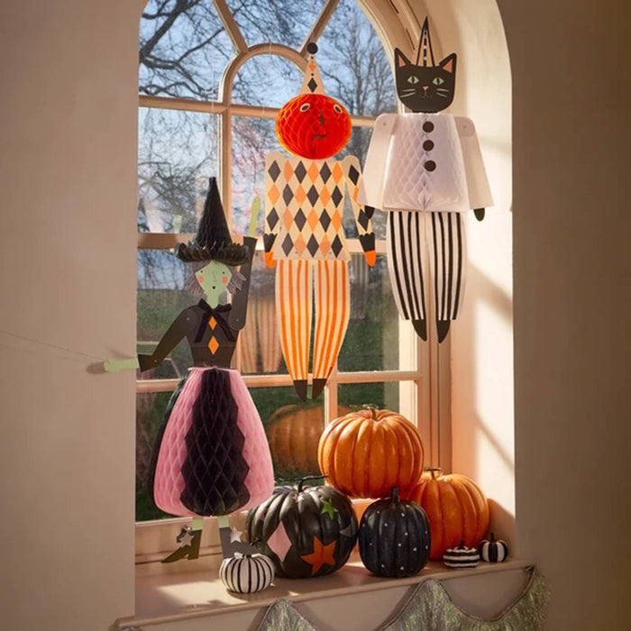 Halloween-themed decorative hanging figures and pumpkins arranged on a windowsill in a real indoor setting with natural window light.