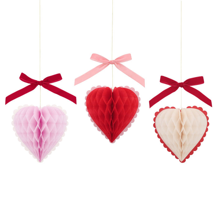 Meri Meri Honeycomb Hearts Valentine's Day decorations, 3 colors of hearts with velvet bows above hanging from gold thread.