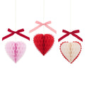 Meri Meri Honeycomb Hearts Valentine's Day decorations, 3 colors of hearts with velvet bows above hanging from gold thread.