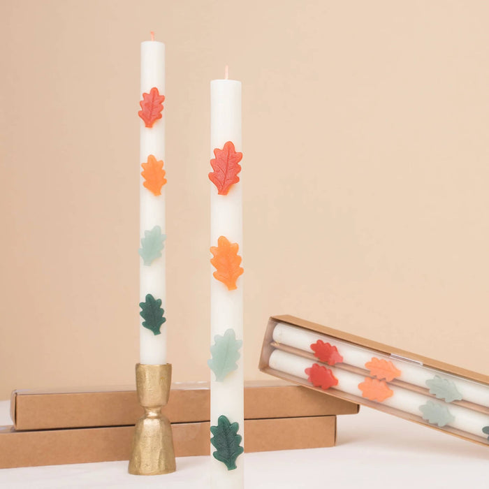Decorative candles with wax autumn leaves in red, orange, yellow, mint, and green, on a beige background.
