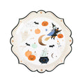A scalloped paper plate featuring cute Halloween illustrations with a witch riding a broomstick, pumpkins, bats, a ghost, a cauldron, and stars on an off-white background, shown on a plain white background.