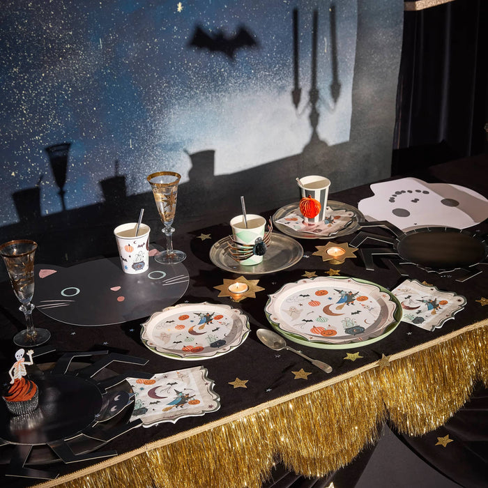 Halloween-themed table setting with decorative plates, cups, and a black tablecloth.