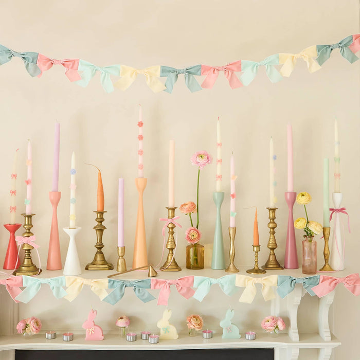 Decorative shelf with pastel candles, flowers, and velvet bow garlands against a beige wall.