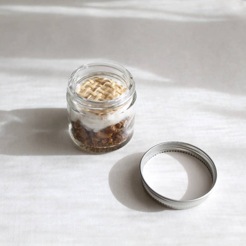 Mom's Me Time aromatherapy inhaler in a glass jar with woven top, lid beside it, on a white surface.