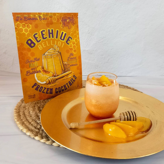 Beehive Bellini frozen cocktail mix package with a glass of cocktail on a gold plate.