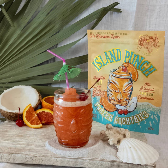 Tropical drink with a straw umbrella and cherry, next to an 'Island Punch' cocktail mix package.