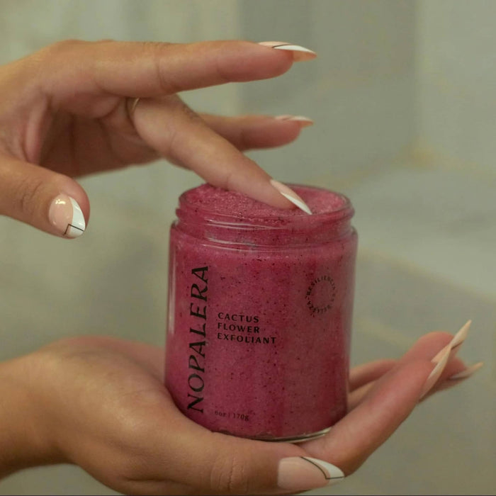 Hand holding a jar of Nopalera hibiscus cactus body polish with a blurred background.
