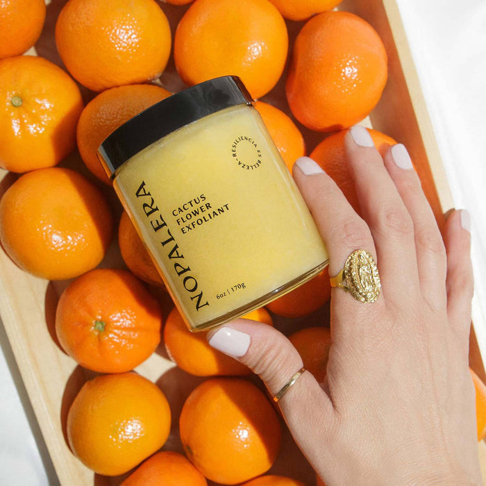 Jar of Nopalera tangerine cactus body polish held over a crate of oranges.