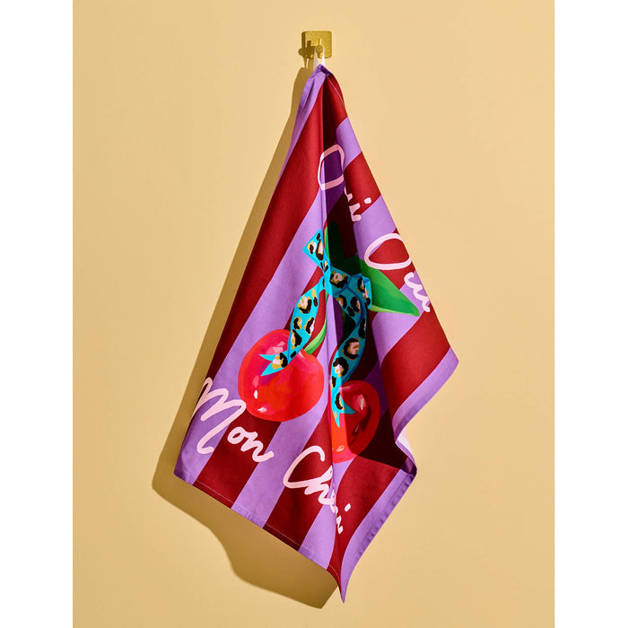 Purple and red striped cotton tea towel with cherries and leopard print bow, featuring text 'Oui Oui Mon Chéri', hanging on a yellow background.