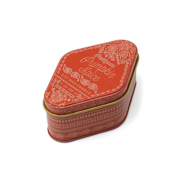 An orange metal tin candle with ornate patterns and the text 'Pumpkin Spice' on the lid, photographed on a clean white background.