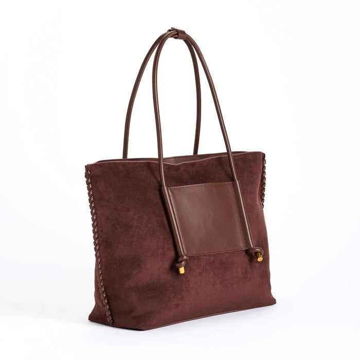 A dark brown vegan suede tote bag with a smooth brown vegan leather front pocket and matching shoulder straps, finished with small gold-tone hardware, front angle view shown against a plain white background.
