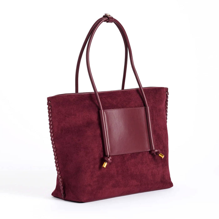 A deep red vegan suede tote bag with a smooth vegan leather front pocket and matching shoulder straps, finished with small gold-tone hardware, front angle view shown against a plain white background.