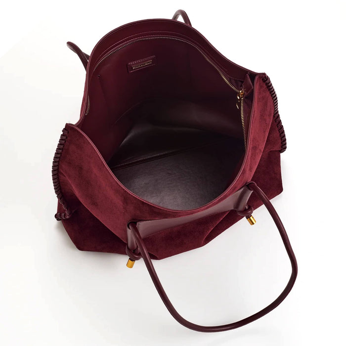 A top-down view of a burgundy vegan suede tote bag with vegan leather handles and gold-tone hardware, shown open on a white background.