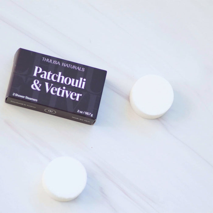 Patchouli & Vetiver scented shower steamers with packaging on a white marble background.