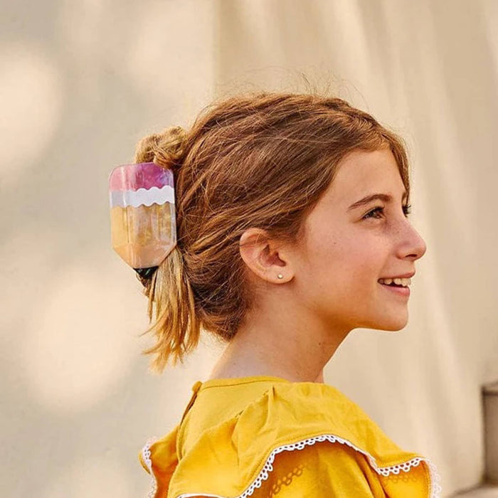 Girl with a pencil-shaped hair clip in her hair against a neutral background.