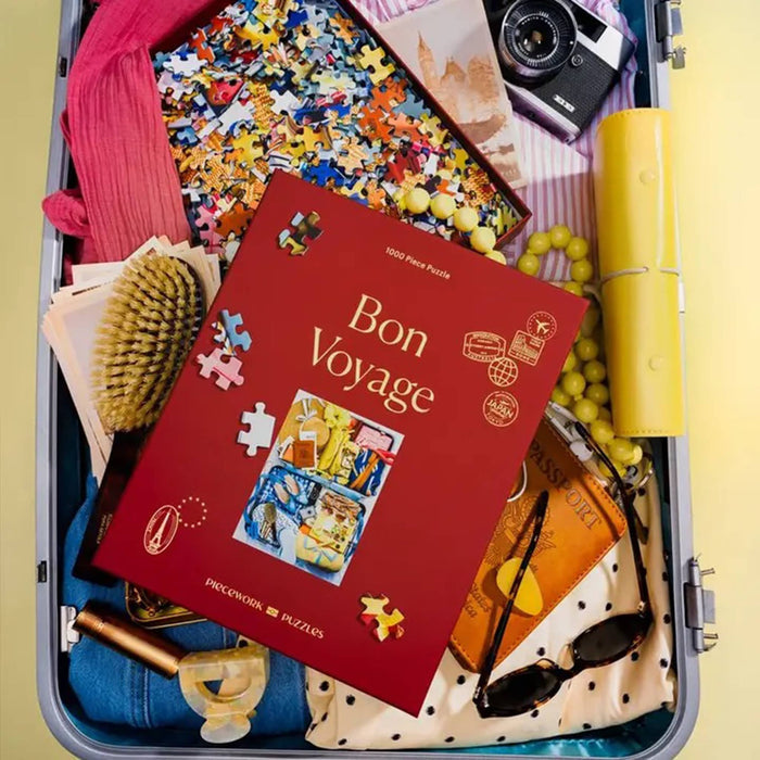 Travel-themed Bon Voyage puzzle in red box packaging, in an open suitcase with travel items, on a yellow background.