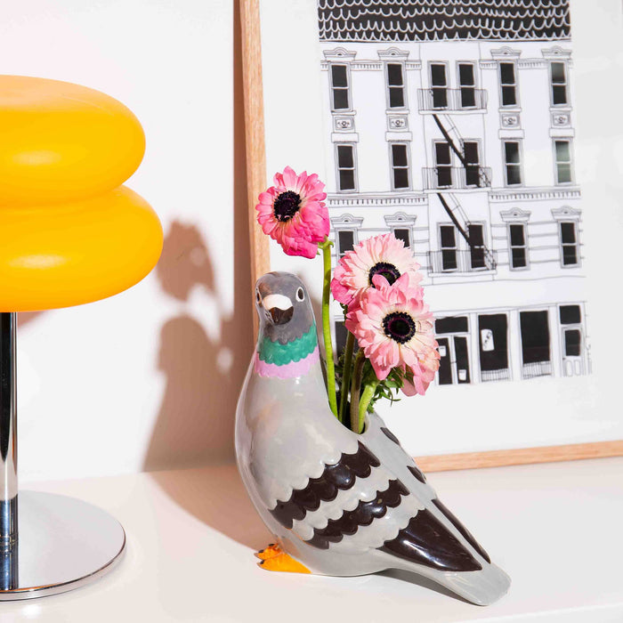 Ceramic pigeon vase on a white table with pink flowers inside.