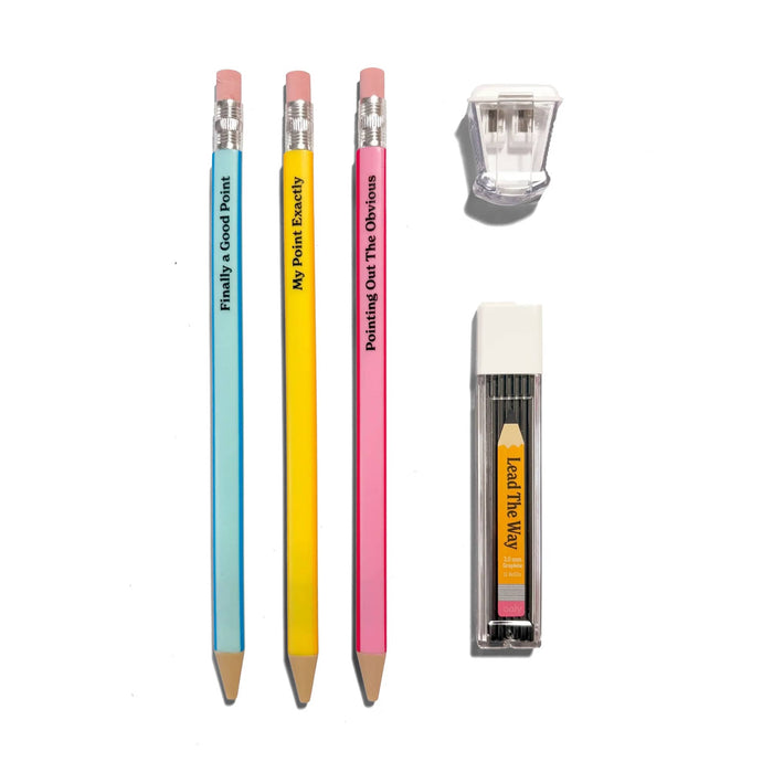 Three colorful mechanical pencils with humorous sayings, a dual-hole pencil sharpener, and a pack of replacement graphite lead, arranged on a clean white background.