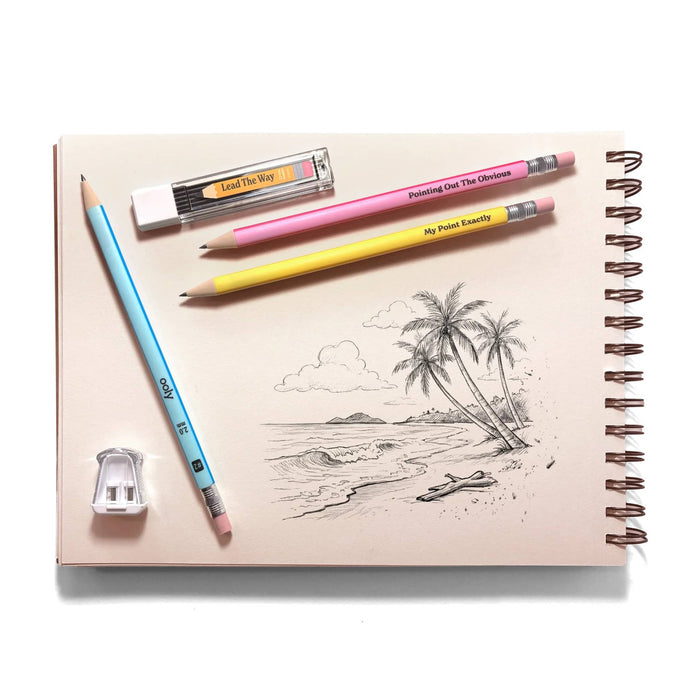 A spiral-bound sketchbook with a black-and-white beach and palm tree drawing, styled with three pencils with colorful barrels, a sharpener, and graphite lead refills on a white background.