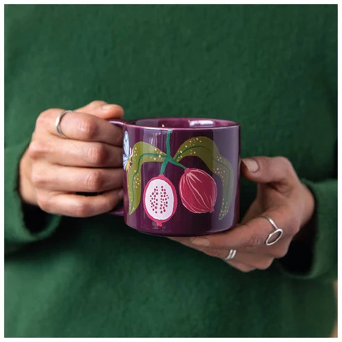 Person holding a dark burgundy mug with fruit illustrations against a green sweater.