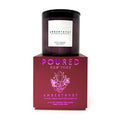 A dark amber glass candle jar with a white label reading AMBERTHYST, displayed on top of a deep red rectangular box with pink foil branding text and crystal illustration. The box reads POURED NEW YORK and AMBERTHYST.