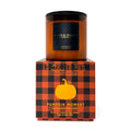 A 10 oz soy coconut candle by Poured New York in the Pumpkin Moment scent, shown with its amber glass jar resting on top of its orange and black buffalo plaid packaging box.