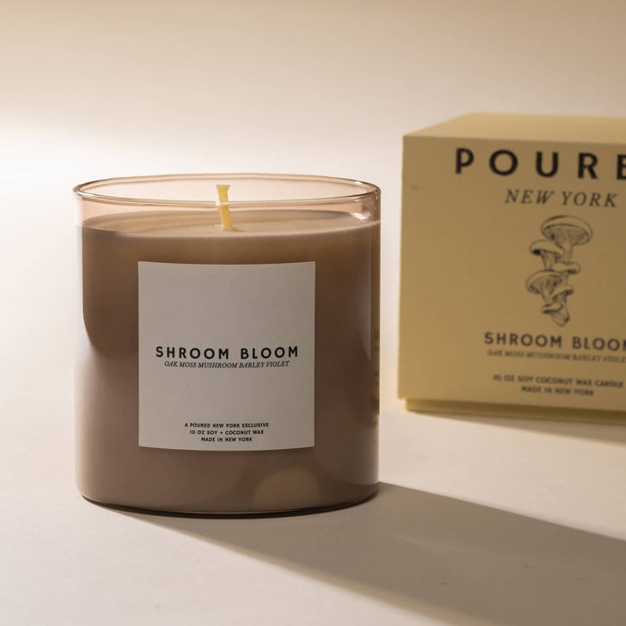 Candle labeled 'Shroom Bloom' with a tan box in the background on a light background.