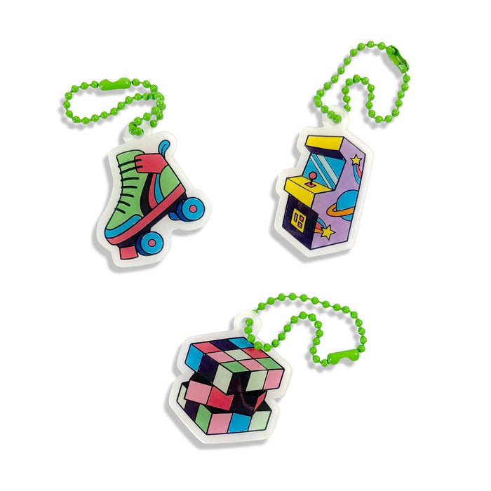 Three colorful novelty keychains on a white background: a roller skate, a retro arcade machine, and a Rubik's cube, each attached to a green bead chain.