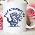 White mug with a blue kitten and flowers design and 'Rage Consumes Me' text, surrounded by pink roses.