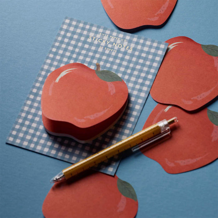 Red apple-shaped sticky notes on a blue gingham sheet, styled with a gold pen on a blue background.