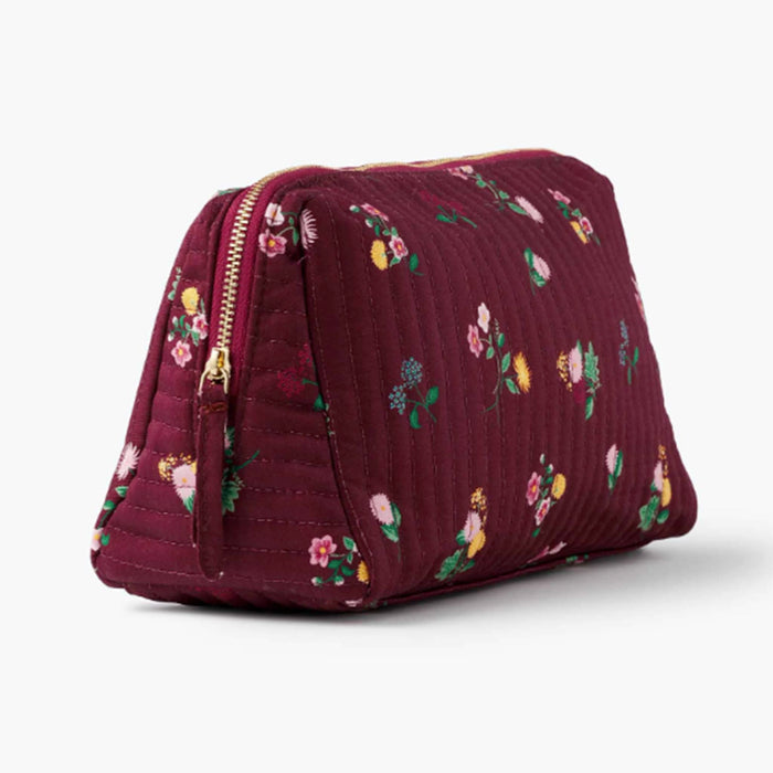 A quilted burgundy cosmetic pouch with a small-scale floral print in pink, yellow, green, and white, and a gold tone zipper, front angle view shown on a plain white background.
