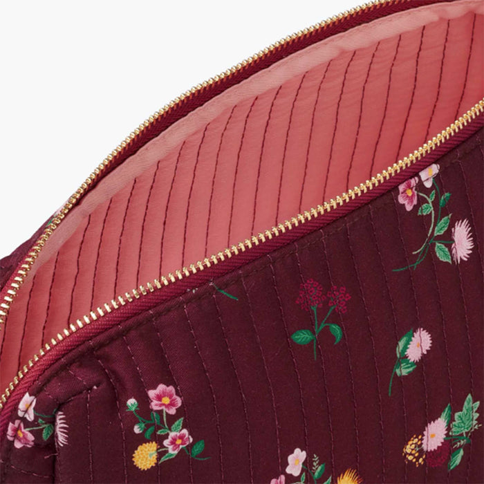 Close-up of a quilted zippered pouch showing a burgundy floral exterior and a pink ribbed interior, with a gold zipper.