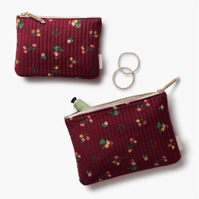 Two quilted burgundy pouches with a small floral print, shown on a light gray background. One pouch is closed, and the other is open, containing a green bottle.