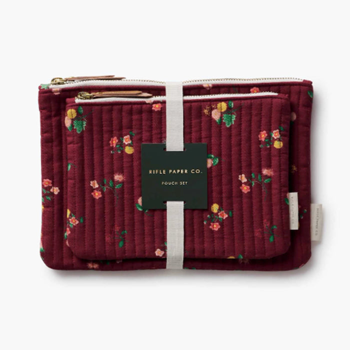 A quilted burgundy pouch set by Rifle Paper Co. featuring a delicate pink, yellow, and green floral pattern, gold-tone zippers, and a central dark green paper label.