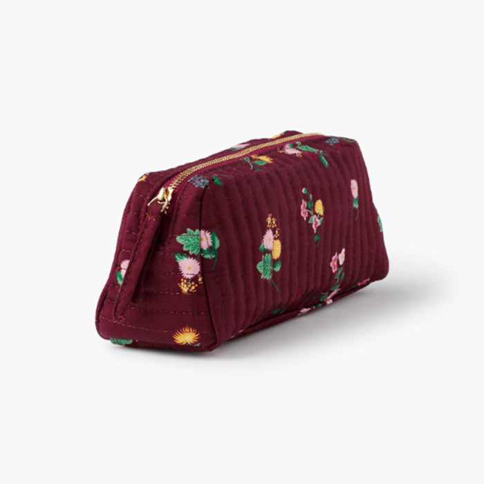 A small quilted burgundy cosmetic pouch with a small-scale floral print in pink, yellow, green, and white, front angle view shown on a plain white background.