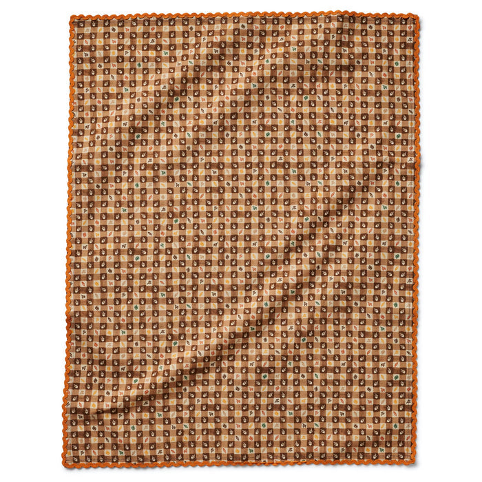 A cotton tea towel with fall harvest icons on a brown gingham backdrop and orange ric-rac trim, shown flat on a white background.