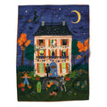 A rectangular tea towel with a Halloween-theme featuring a whimsical illustration of a haunted house at night, with pumpkins, bats, a crescent moon, stars, and characters in front of the door. The design has a dark navy sky, orange trees, and a cream house, with an orange ric-rac border along the edges.