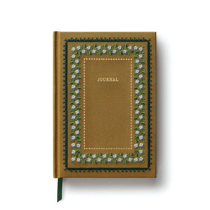 A hardcover journal with a textured mustard-yellow cover, featuring a decorative border of white flowers and green leaves, with the word 'JOURNAL' printed in gold in the center. A dark green ribbon bookmark is visible at the bottom left.
