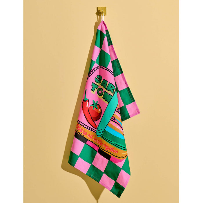 Green and pink checkerboard cotton tea towel with a sardine tin illustration, hanging against a yellow background.