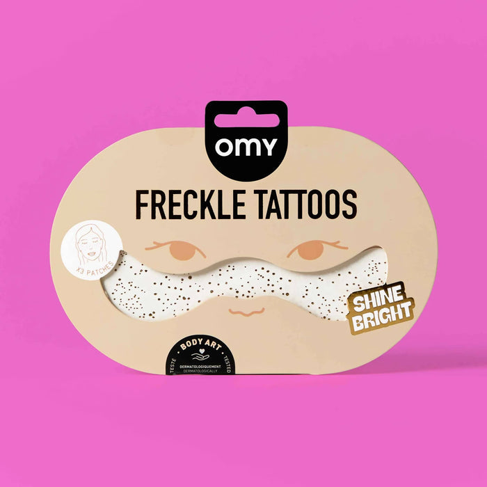 Packaging of gold freckle tattoos with 'omy' branding on a pink background.