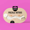 Packaging of gold freckle tattoos with 'omy' branding on a pink background.