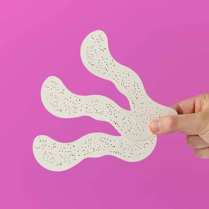 Hand holding 3 sheets of gold freckle temporary tattoos against a pink background.