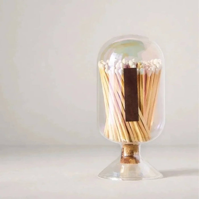 Back of a clear glass cloche with an iridescent finish lid containing wooden safety matches, with a striker strip on the back, photographed on a white background.