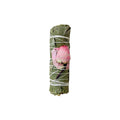 Dried eucalyptus smudge bundle with a dried pink rose, tied up with cotton string, on a white background.