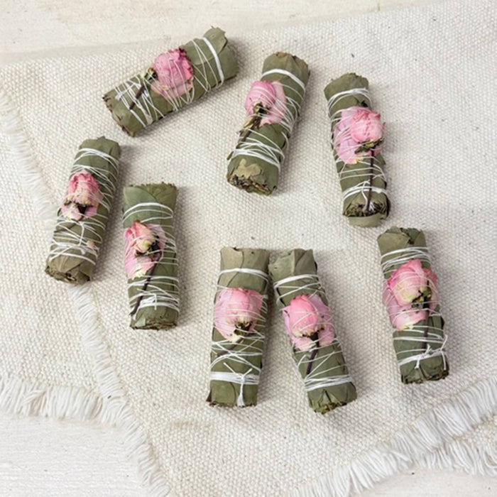 Dried eucalyptus smudge bundles with a dried pink rose, tied up with cotton string, on a textured cream background.