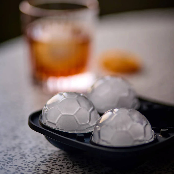 Gentlemen's Hardware The Beautiful Game collection soccer ball shaped ice mold with finished cubes and an old fashioned glass in the background.