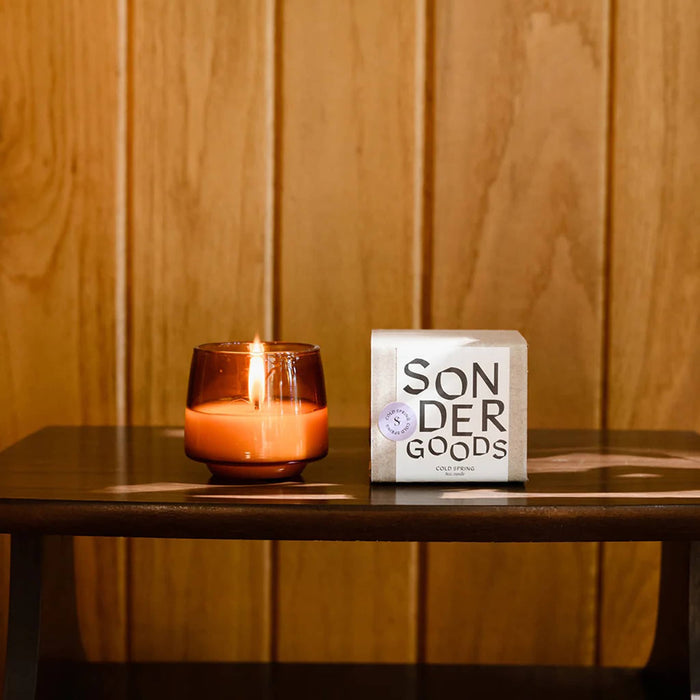 Candle and 'Sonder Goods' box on a wooden surface with a wooden panel background.