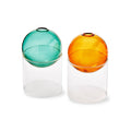 Two translucent glass vases with spherical tops in green and amber, each resting on a clear cylindrical base, photographed on a white background.