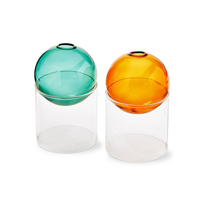 Two translucent glass vases with spherical tops in green and amber, each resting on a clear cylindrical base, photographed on a white background.