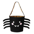 A black spider-shaped Halloween bucket bag with a smiling face, pink cheeks, and eight black legs, featuring an orange and black striped handle on a white background.
